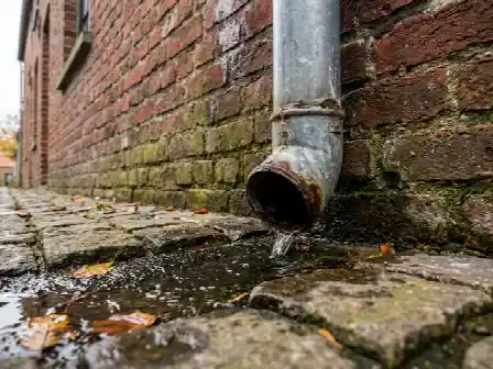 Regenpijp die aan de voet van een vochtige gevel loost